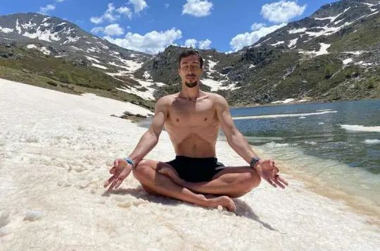 Mann meditiert im Schneidersitz an einem Bergsee